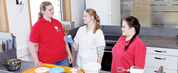 Anleiterin zeigt Auszubildenden die Zutaten beim Backen.