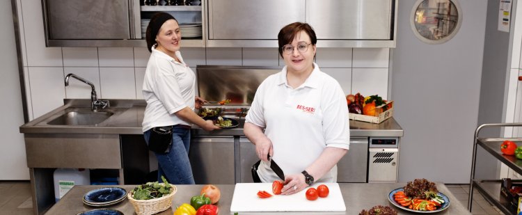 Zwei Mitarbeiterinnen schneiden Gemüse für einen Salat.