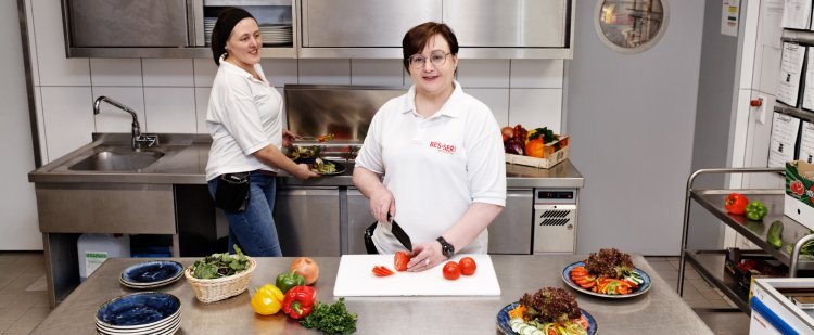 Zwei Mitarbeiterinnen schneiden Gemüse für einen Salat.
