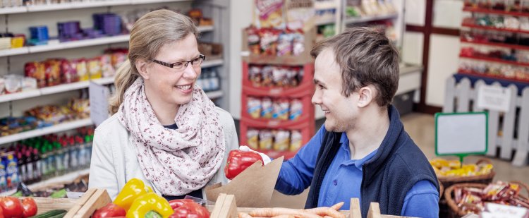 Kauffrau im Einzelhandel und Beschäftigter im Laden hinter Gemüsekisten.