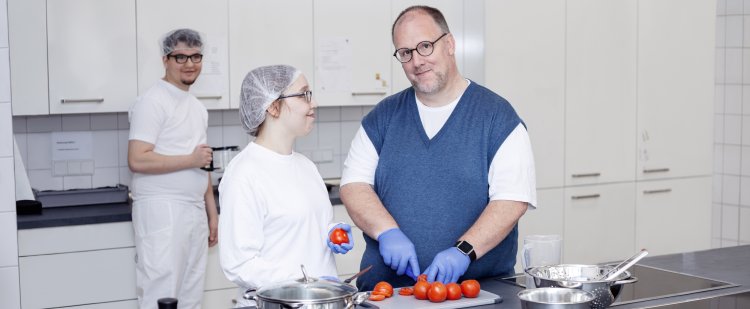 Koch und Beschäftigte schneiden Tomaten in Großküche.