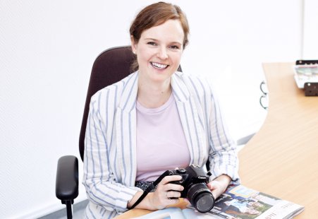 Marketing-Fachkraft sitzt am Schreibtisch und hält Kamera.