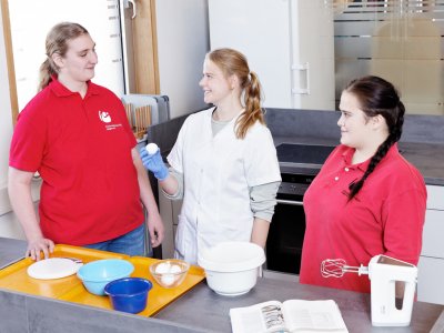 Anleiterin zeigt Auszubildenden die Zutaten beim Backen.