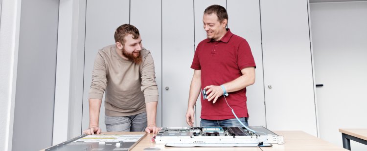 Anleiter erklärt Auszubildendem einen Serverkasten.