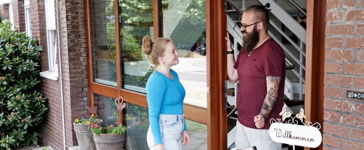 Mitarbeiter nimmt Jugendliche an der Haustür in Empfang. Bei ihnen sitzt ein Hund.