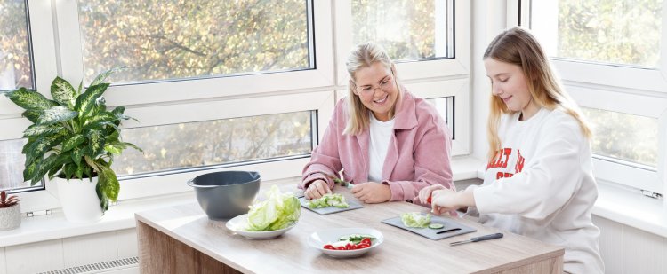 Mitarbeiterin und Jugendliche schneiden Gemüse.