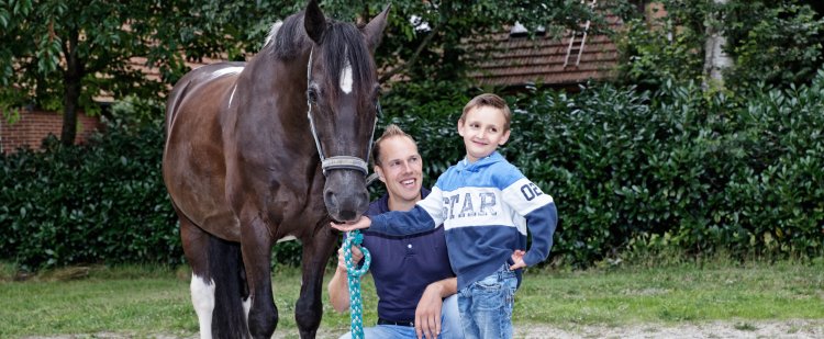 Kind füttert ein Pferd. Betreuer kniet daneben.