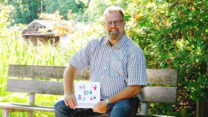 Logopäde sitzt auf Bank im Grünen.