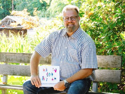 Logopäde sitzt auf Bank im Grünen.