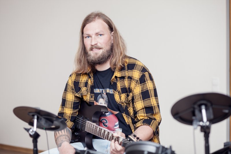 Erzieher sitzt mit Gitarre im Schoß am Schlagzeug.
