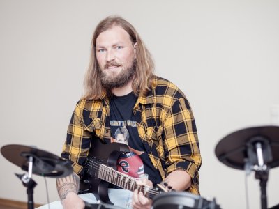 Erzieher sitzt mit Gitarre im Schoß am Schlagzeug.