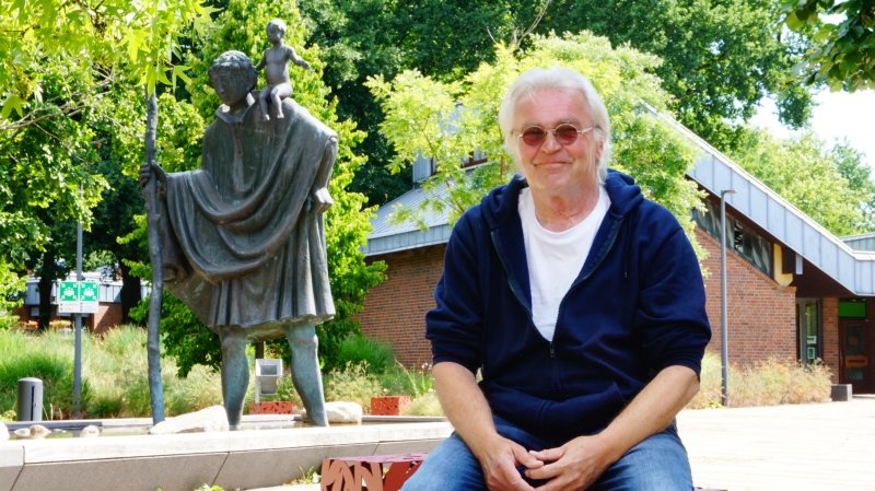 Mann sitzt draußen vor Christophorus-Statur.