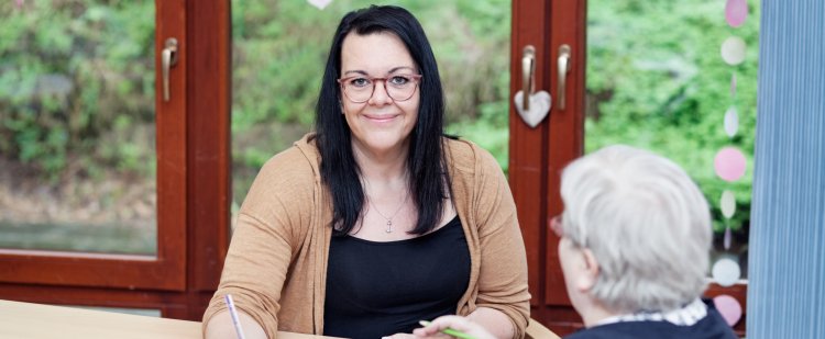 Altenpflegerin und ältere Frau sitzen am Tisch und malen ein Bild.