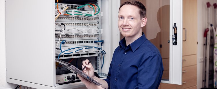 IT-Fachinformatiker steht mit Tablet vor geöffnetem Serverschrank.