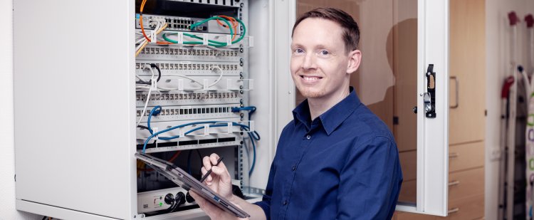 IT-Fachinformatiker steht mit Tablet vor geöffnetem Serverschrank.