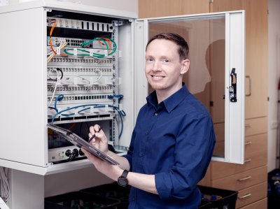 IT-Fachinformatiker steht mit Tablet vor geöffnetem Serverschrank.
