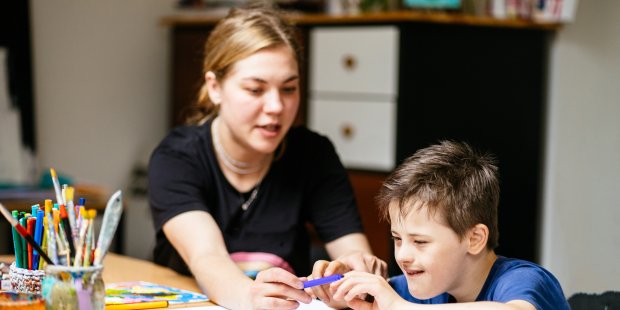 Betreuungskraft hilft Jungen beim Malen eines Bildes.