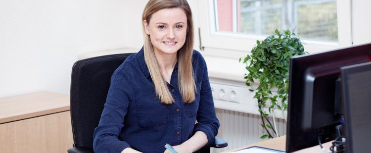 Kauffrau für Büromanagement sitzt am Schreibtisch und schreibt in eine Mappe.