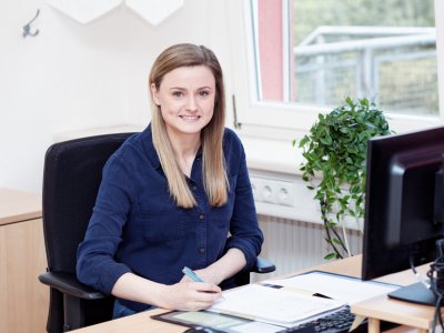 Kauffrau für Büromanagement sitzt am Schreibtisch und schreibt in eine Mappe.