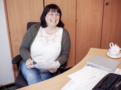 Kauffrau für Büromanagement sitzt am Schreibtisch und hält Zettel und Papier.