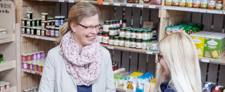 Kauffrau im Einzelhandel und Beschäftigte vor Ladenregal mit Verpackungen in den Händen.