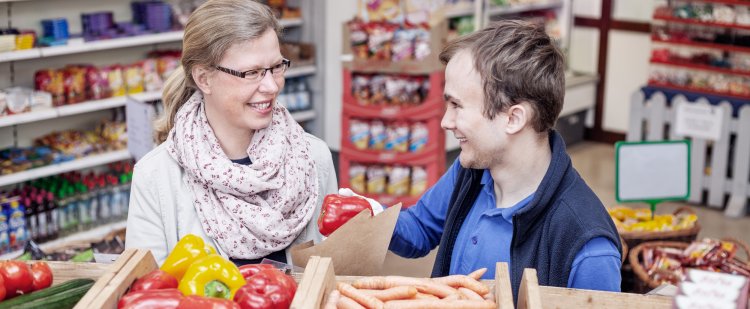 Kauffrau im Einzelhandel und Beschäftigter im Laden hinter Gemüsekisten.