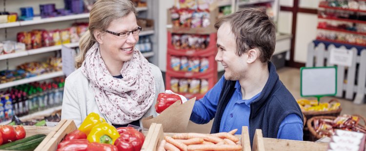 Kauffrau im Einzelhandel und Beschäftigter im Laden hinter Gemüsekisten.