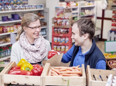 Kauffrau im Einzelhandel und Beschäftigter im Laden hinter Gemüsekisten.