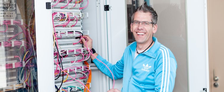 Elektrotechniker steht vor offenem Serverschrank und hält ein Kabel in der Hand.