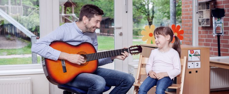 Erzieher spielt Mädchen auf der Gitarre vor.