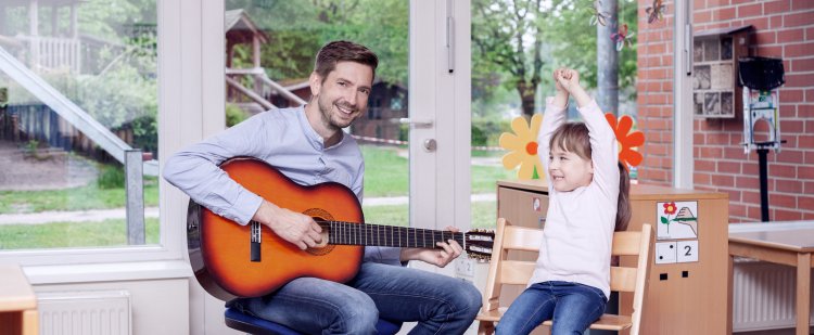 Erzieher spielt Mädchen auf der Gitarre vor.