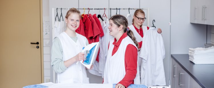 Hauswirtschafterin steht mit Beschäftigter an einem Bügelbrett und hält ein Bügeleisen.