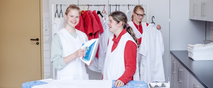 Hauswirtschafterin steht mit Beschäftigter an einem Bügelbrett und hält ein Bügeleisen.