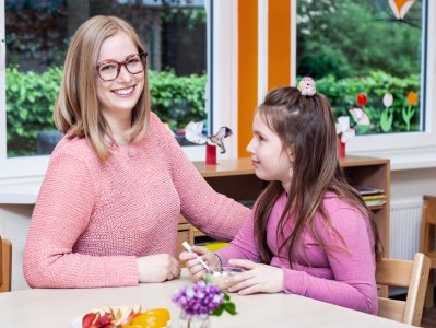 Heilerziehungspflegerin betreut Mädchen beim Essen.