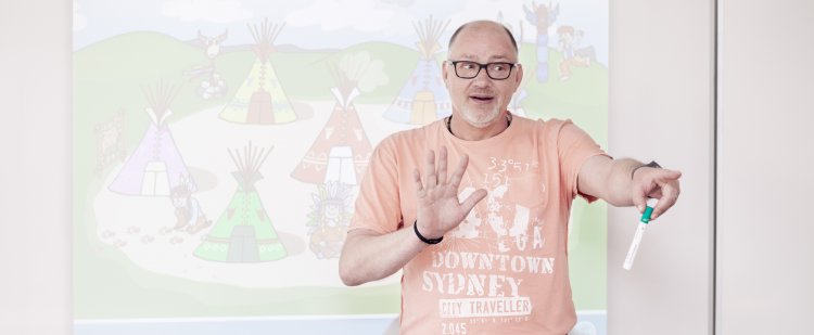 Heilpädagoge steht mit Stift in der Hand vor Whiteboard und zeigt in den Raum.