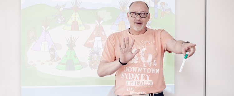 Heilpädagoge steht mit Stift in der Hand vor Whiteboard und zeigt in den Raum.