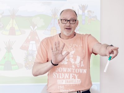 Heilpädagoge steht mit Stift in der Hand vor Whiteboard und zeigt in den Raum.