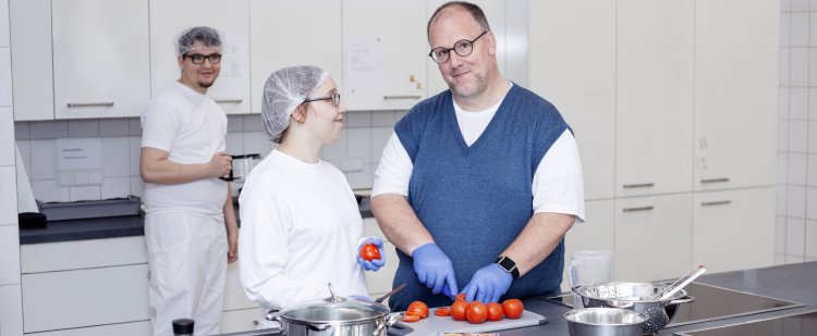Koch und Beschäftigte schneiden Tomaten in Großküche.