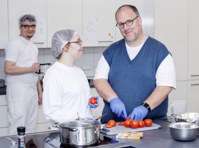 Koch und Beschäftigte schneiden Tomaten in Großküche.
