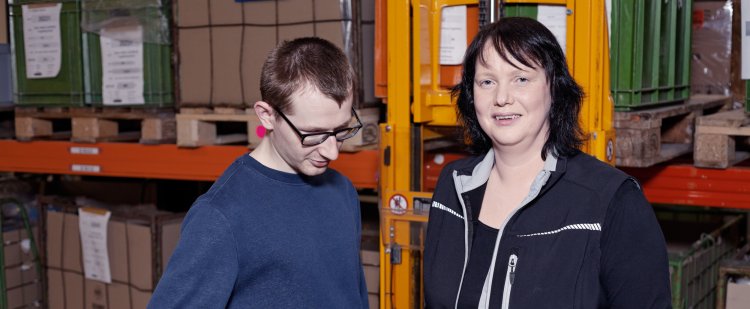Wirtschaftswirtin zeigt einem Beschäftigten die Bedienung eines Handhubwagens.
