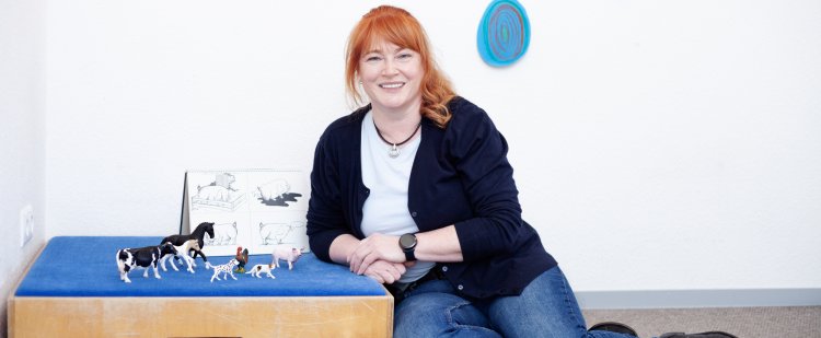 Logopädin kniet neben Kasten mit Spielzeug-Tieren.