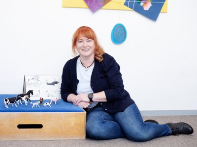 Logopädin kniet neben Kasten mit Spielzeug-Tieren.