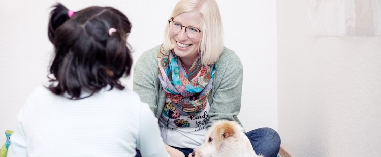 Logopädin, Mädchen und Therapiehund sitzen auf dem Boden.