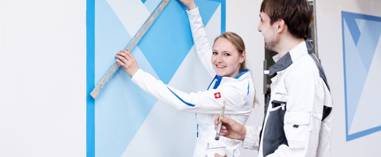 Maler- und Lackiererin und Beschäftigter malen ein blaues Muster auf eine weiße Wand.