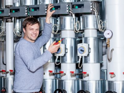 Sanitär- und Heizungsbauer steht mit Schraubenzieher vor großer Heizungsanlage.