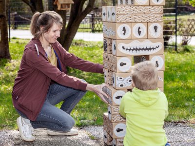 Sozialpädagogin spielt mit Kind im Garten an Turm aus großen Holzklötzen.
