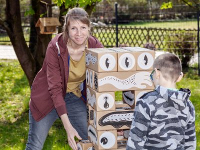 Sozialpädagogin spielt mit Kind im Garten an Turm aus großen Holzklötzen.