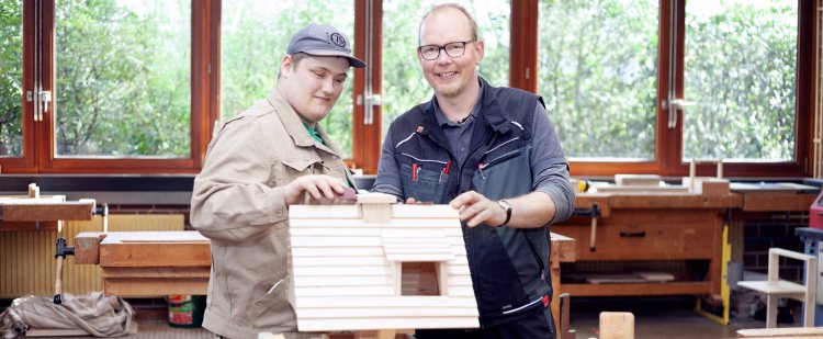 Tischler und Beschäftigter schmirgeln Vogelhaus in Holzwerkstatt.