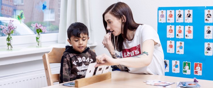 Auszubildende sitzt mit Jungen an einem Tisch und nutzt Karten für Sprechübungen.