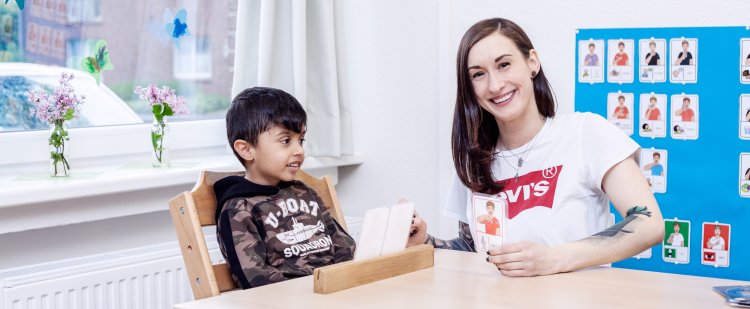 Auszubildende sitzt mit Jungen an einem Tisch und nutzt Karten für Sprechübungen.